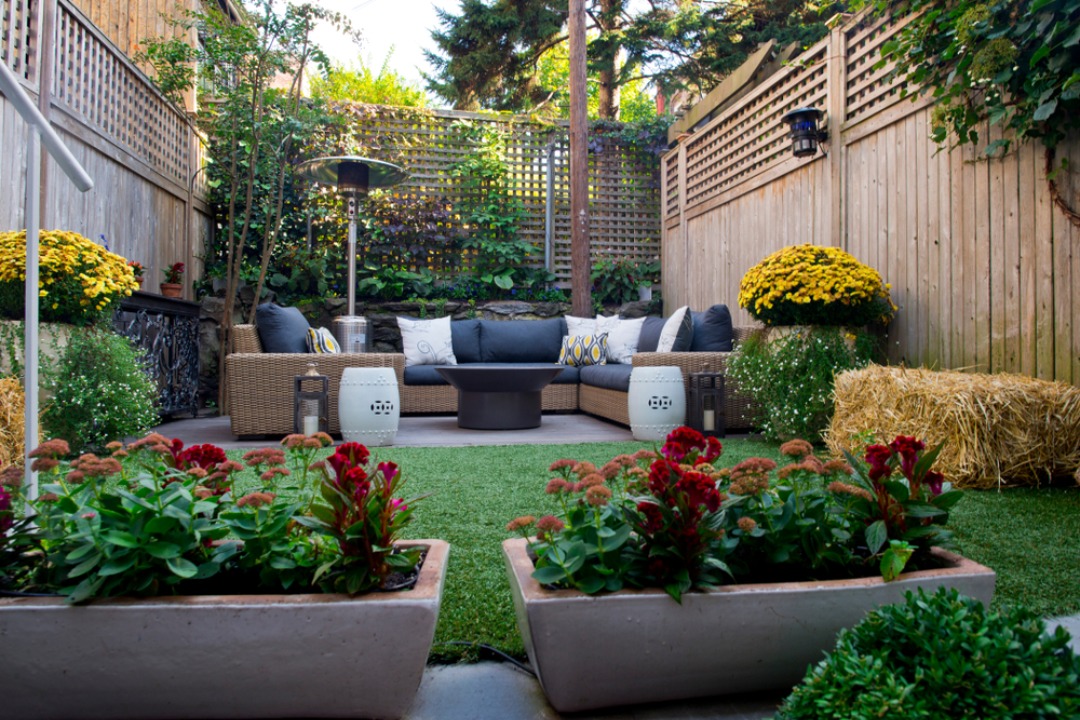 A charming backyard lounge with wicker seating, potted plants, and a fire pit creates a cozy outdoor living space.