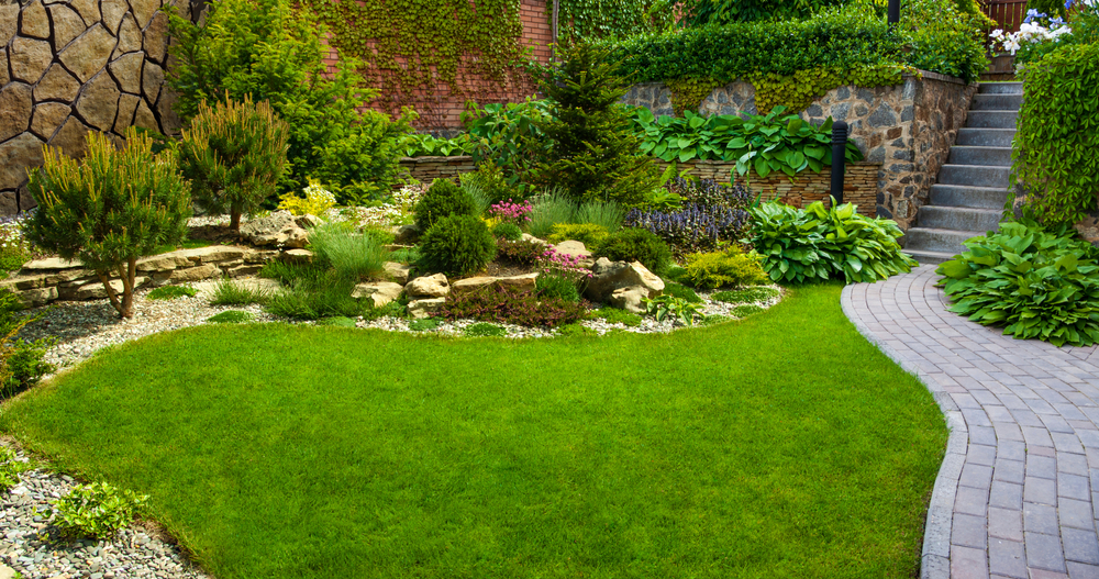 A beautifully designed garden with lush green grass, a stone pathway, and various plants arranged for a natural landscape.